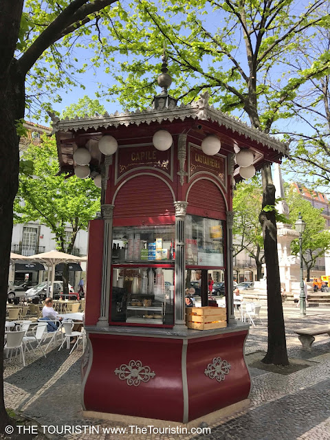 A café with outdoor seating under trees in a tiny red pavilion.