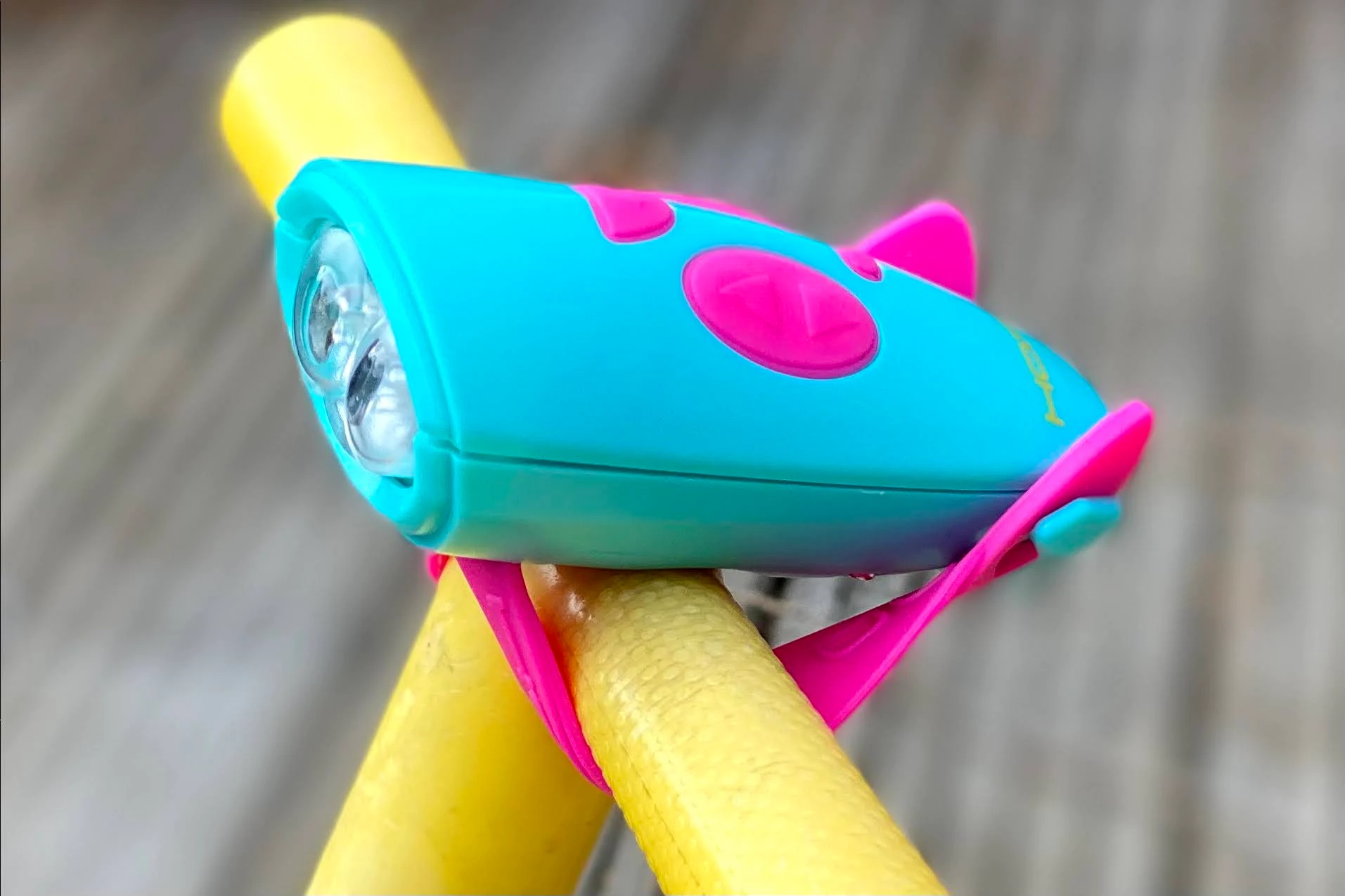 a pink and turquoise hornit mini light and noise maker on the handle bars of a yellow bumblebee scuttlebug
