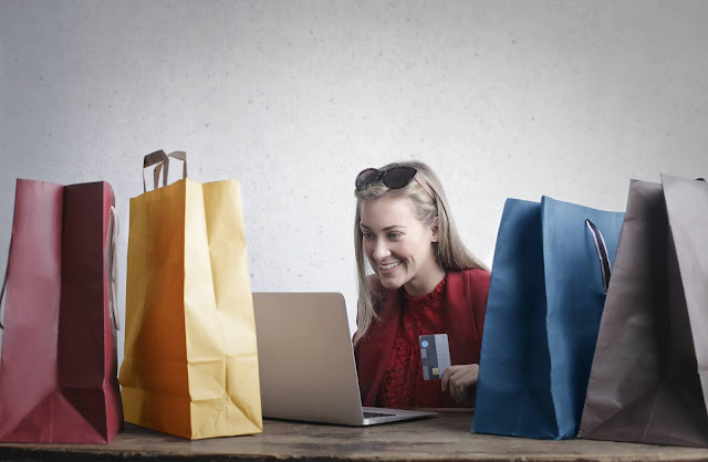 Blonde girl holding a credit card and smiling in front of her laptop.