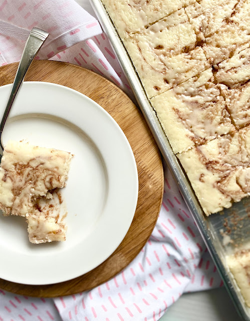 Slice of cinnamon roll cake on a white plate next to a sheet pan.