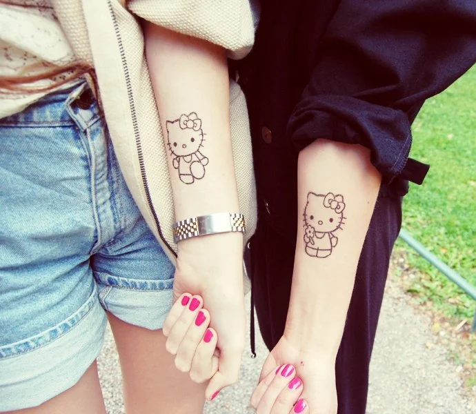 dos brazos de dos adolescentes, vemos en cada uno un tatuaje de hello kitty