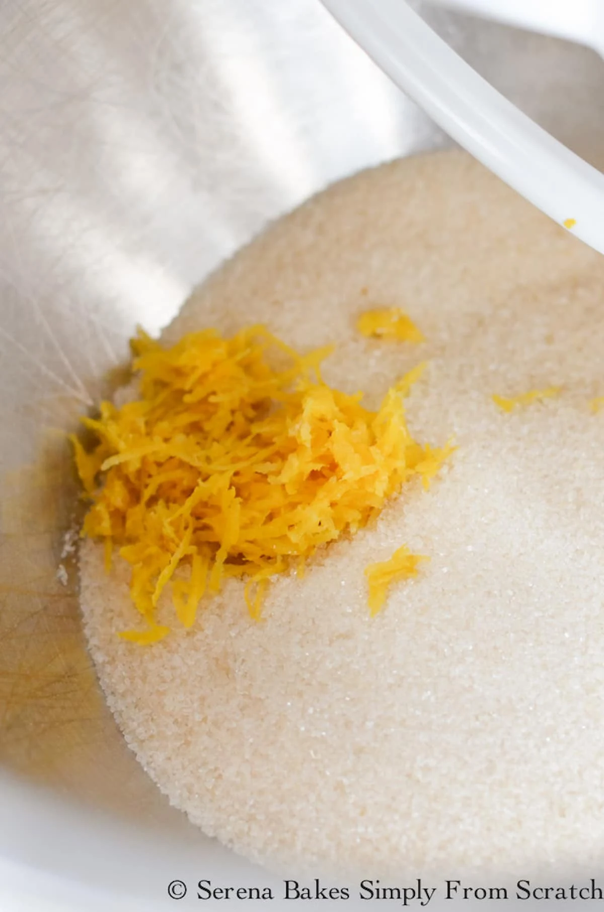 Sugar and Grated Lemon Zest in a stainless steel mixing bowl.