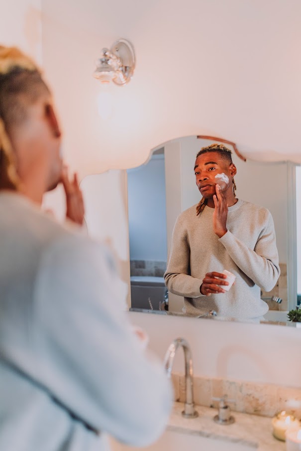 Mies laittaa ihonhoitotuotetta kasvoihinsa peilin edessä