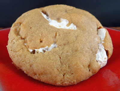 A single peanut butter cookie, molded around a filling of marshmallow fluff, which peaks through the cookie dough in several places. Photographed on a red plate.