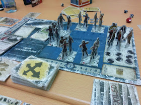 The game board in progress. The main game board has several human characters in the shelter, surrounded by a number of zombies.