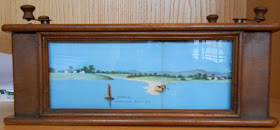 The lighthouse on water, positioned behind glass in a wooden frame.