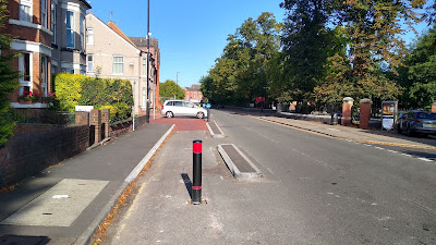 A skinny traffic island set out from the left hand kerb of a street to start a carriageway-level two-way cycle track.