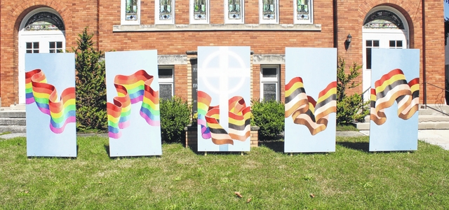 Mural shows a rainbow ribbon coming from the left and a racial harmony flag coming from the right, to join around a cross in the center panel. Located at Peace Community Church in Oberlin; mural by Robert Cothran (photo by VUrbanik).