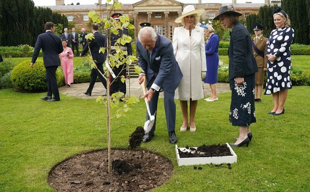 Queen Camilla wore a blue midi dress. The Queen wore an ivory two-tone coat and white midi dress. Coronation Garden in Newtownabbey