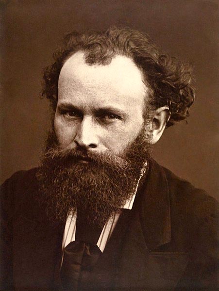 black-and-white photo of a man with bushy hair and a bushy beard, and heavy brows, and wearing a dark suit