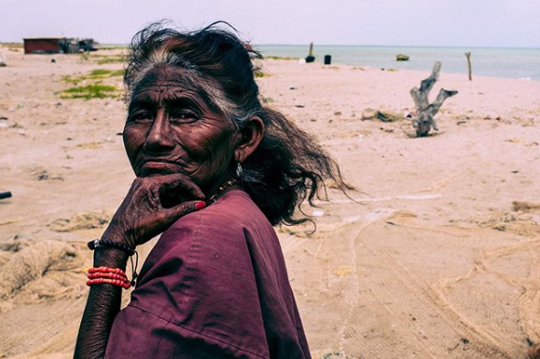 Senhora Colombiana, posa para foto, ela tem a pele enrugada e cabelos grisalhos amarrados. 