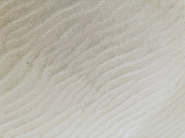 A foto mostra a areia do mar cheia de ondulações causadas pelas ondas.