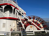 A photo of the steamboat docked along the New Orleans Waterfront. It says "City of New Orleans' on the stern. The paddlewheel is visible.