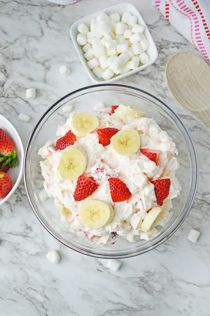 Strawberry Banana Cheesecake Fluff Salad in a clear glass bowl garnished with strawberries and bananas.