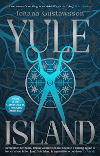 Book "Yule Island" by Johana Gustawsson. A pair of scissors, open and points down, in a chilly blue with the device of a skull in the centre. Behind them, a circle divided into eight parts by a repeated, cryptic symbol. There is a snowflake in each section. Behind all this, curving lines which might be branches, or possibly cracks in ice.