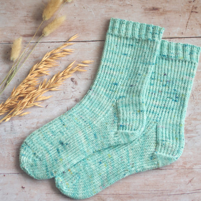 seafoam handnit socks with allover slipped stitch pattern laid flat with dried grass