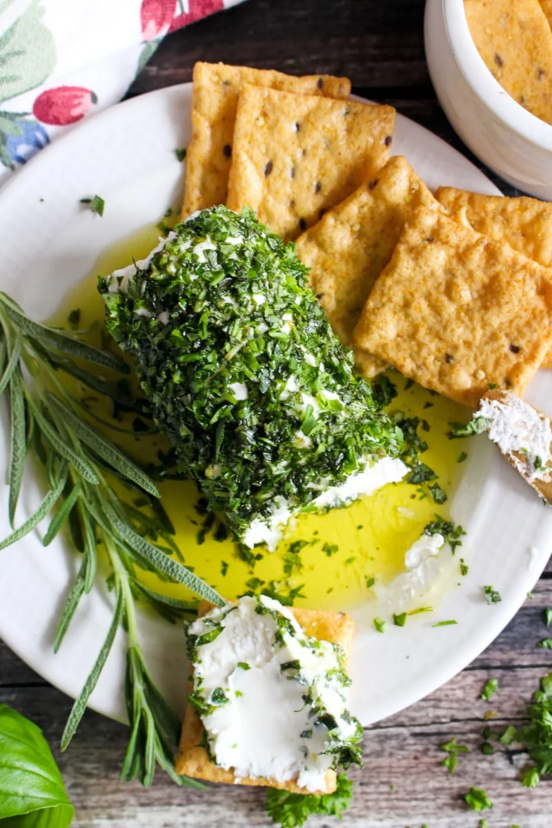 Top view of Herb and Olive Oil Goat Cheese Log on a cream colored plate with crackers next to it.