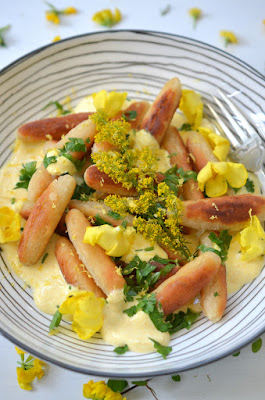 Mühlviertler Sonnwendnudeln sind auf einem Teller mit gelb gefärbter Sauerrahmcreme angerichtet und mit Blüten und gehackter Petersilie garniert.