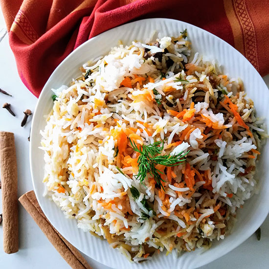 Plate of Madras chicken biryani on an orange red napkin with cinnamon sticks and cloves on table