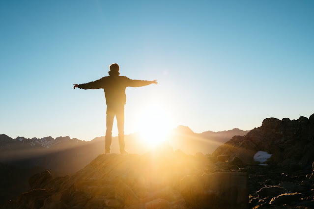 We see the light at the end of the tunnel with the COVID-19 vaccines.  Image shows man standing on top of a hill looking at the sunlight.