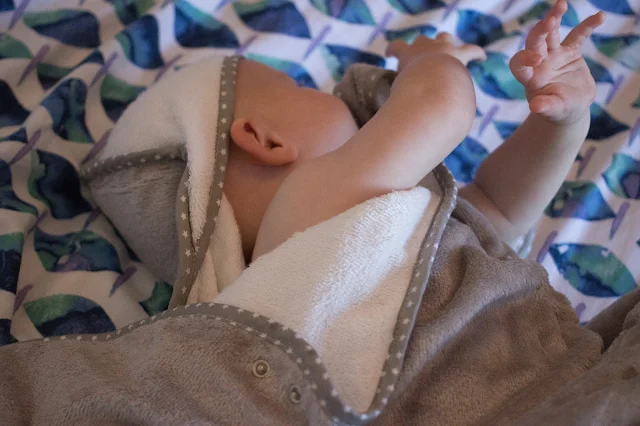 A baby wrapped up on a bed in the Cuddledry original baby towel in grey stars and white