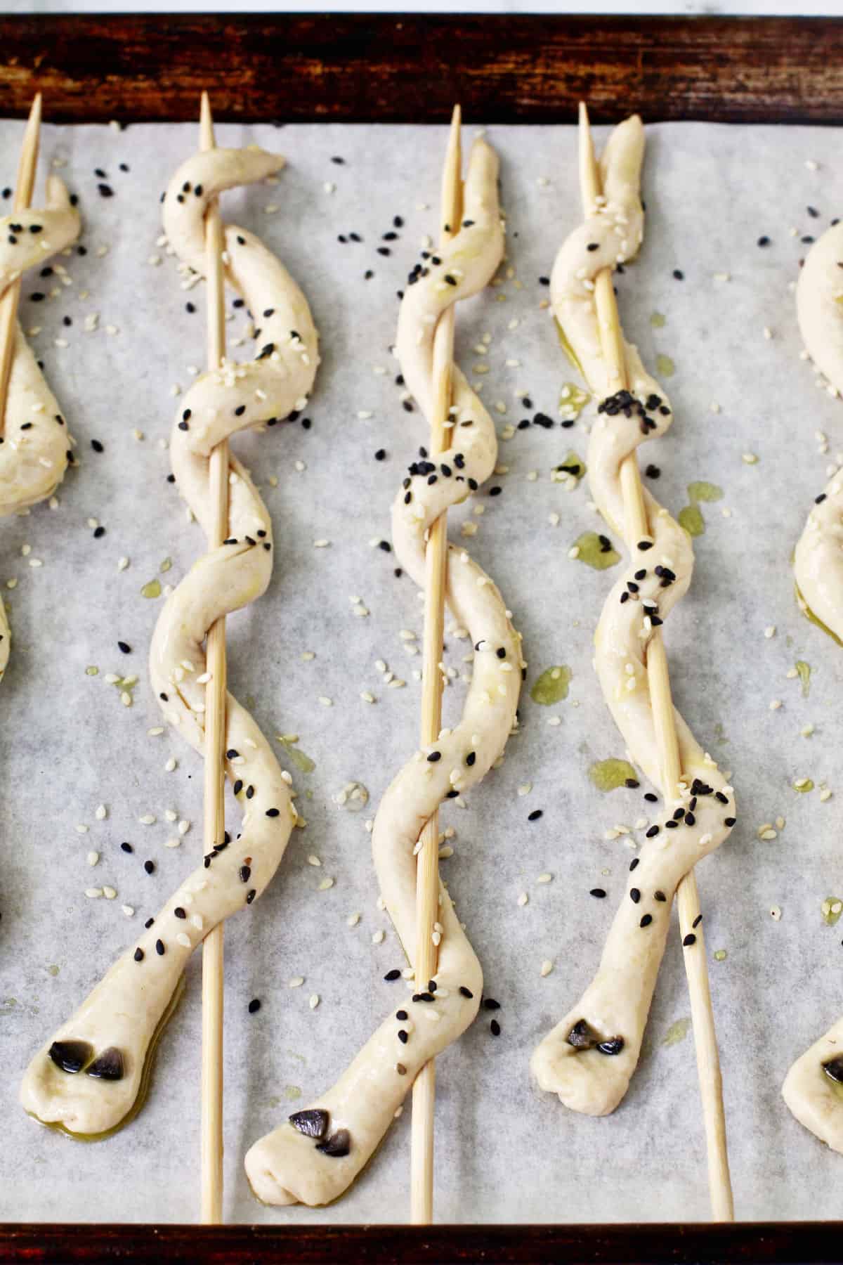 Breadstick Snakes before baking wrapped around wooden skewers and decorated with sesame seeds.