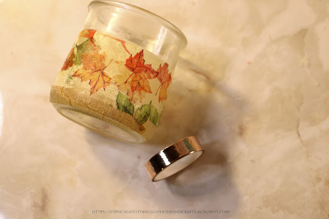 A glass jar with decorative napkin on it with decorative tape beside it
