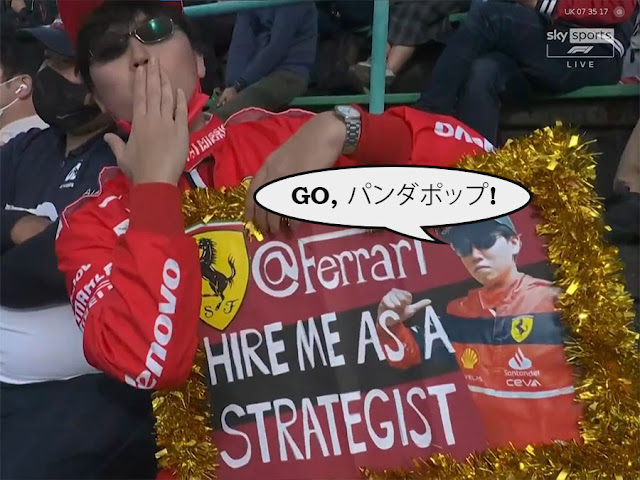 A Japanese F1 fan with a sign saying "Ferrari, hire me as a strategist" with the added caption "Go, パンダポップ"