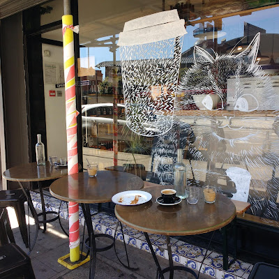 Cafe window with images of coffee cup and cat that look like they could have been drawn by Louis Wain