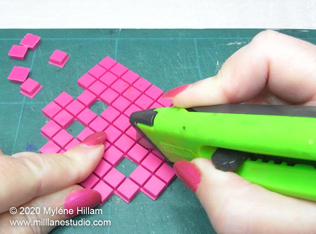 Square of pink pixels being trimmed with a craft knife to the shape of a space invader