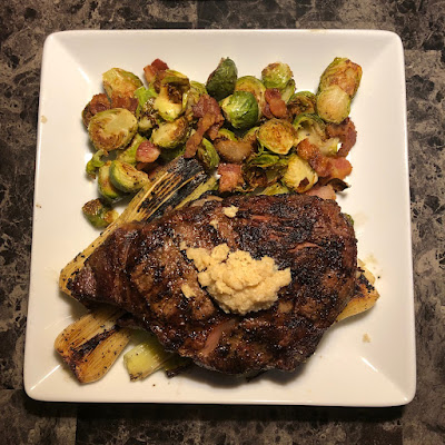 Prime ribeye grilled rare with some grilled leeks, bacon roasted Brussels sprouts