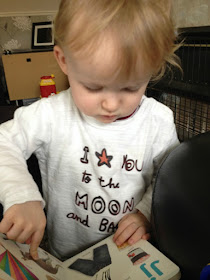 toddler pointing at picture in book and wearing t shirt that says I love you to the moon and back.