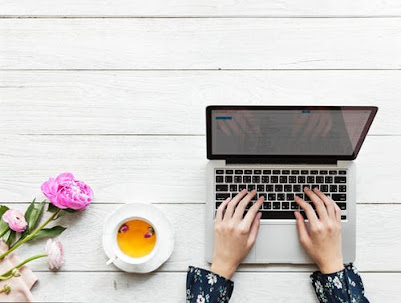 A person marketing from a computer, with flowers and a mug of beverage on the table.