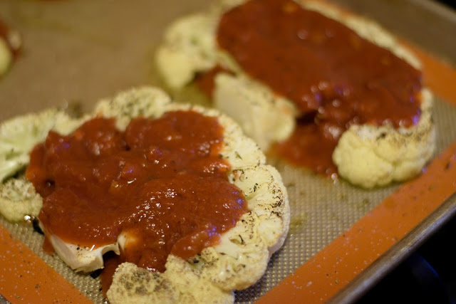 Marinara sauce being spooned over the roasted cauliflower steaks.  