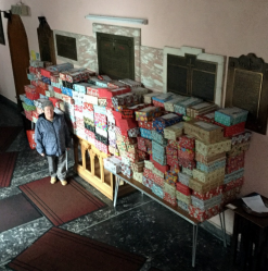 A lady stood next to a large table that is covered in shoe box size Christmas gifts