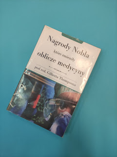 Na niebieskim tle znajduje się okładka książki> Książka ma napis Nagrody Nobla które zmieniły oblicze medycyny oraz twarz naukowca w maseczce