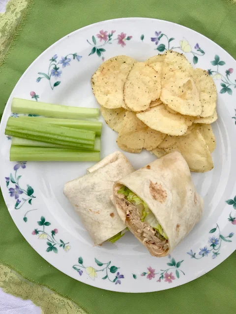 Slow cooker Buffalo chicken wrap on a plate with celery and chips.