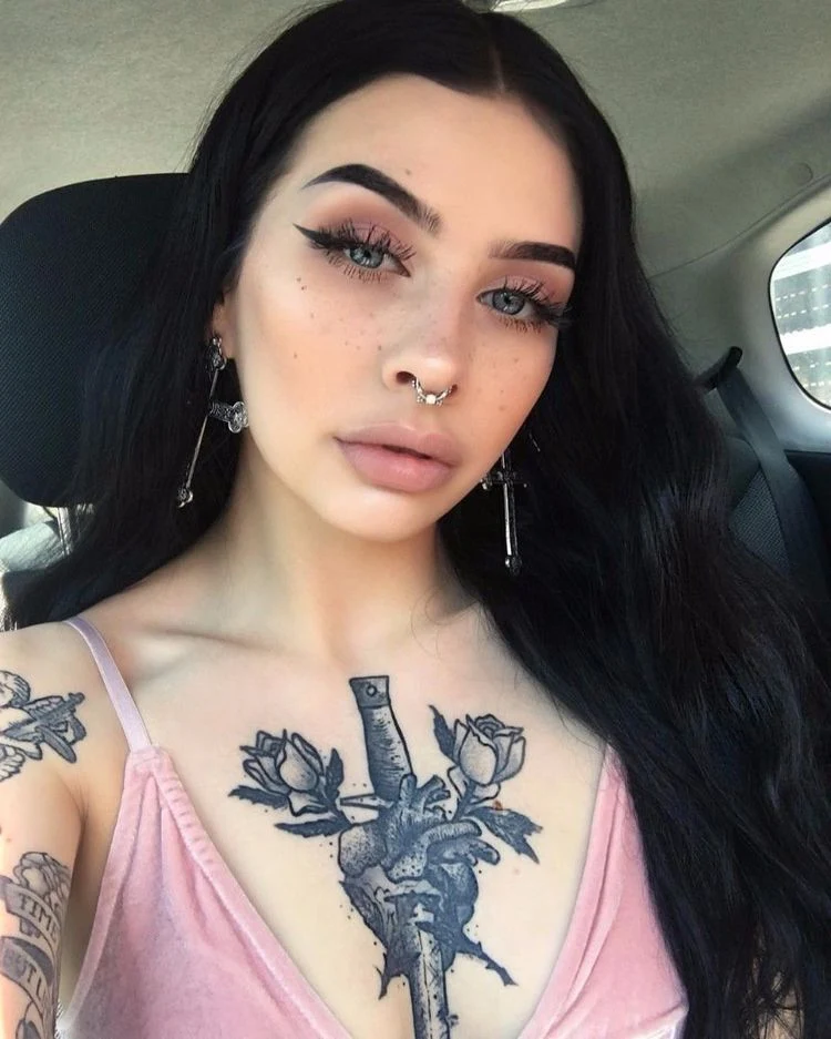 Preciosa mujer latina de piel clara en su auto, lleva un tatuaje de una daga y flor en el pecho, muy sensual si señor