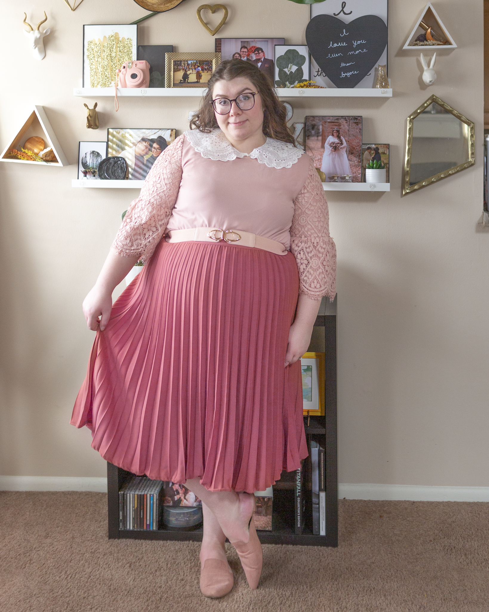 An outfit consisting of a pastel pink dress with lace sleeves tucked into a rose colored pleated midi skirt and muted pink pointed toe mules.