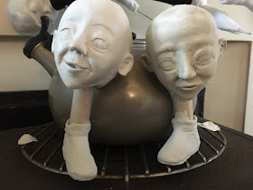 two sculpted heads drying on a stove, each resting on a sculpted lower leg. By Artist Corina Duyn