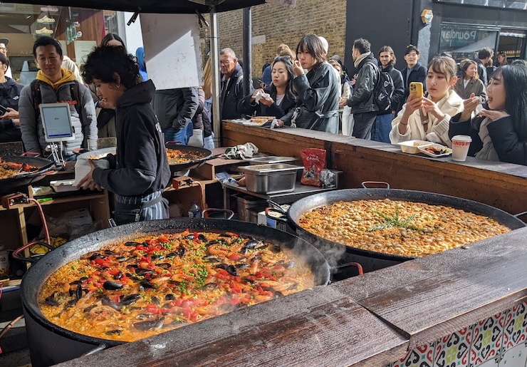 Huge pans of paella simmer at an open-air booth at a street market