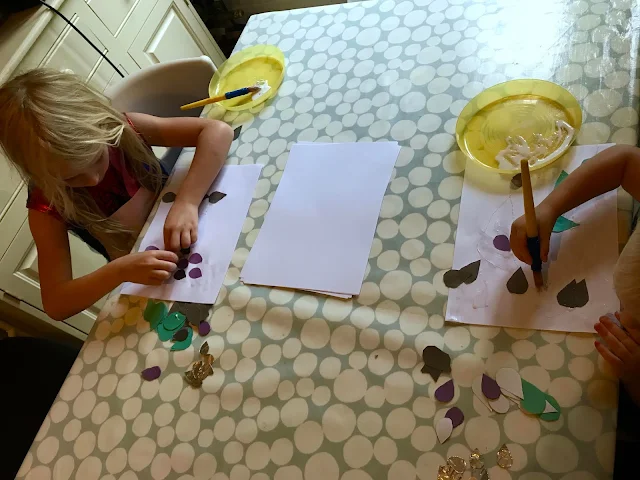 An overhead view of a table with a toddler and 6 year old sticking rainbow shapes to paper