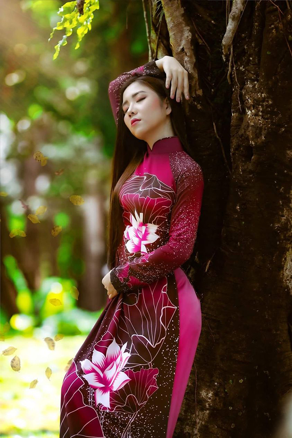 Thiếu nữ áo dài đỏ hoa đứng tựa cây