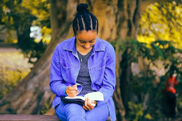 A young lady seated under a tree coach reading her Bible