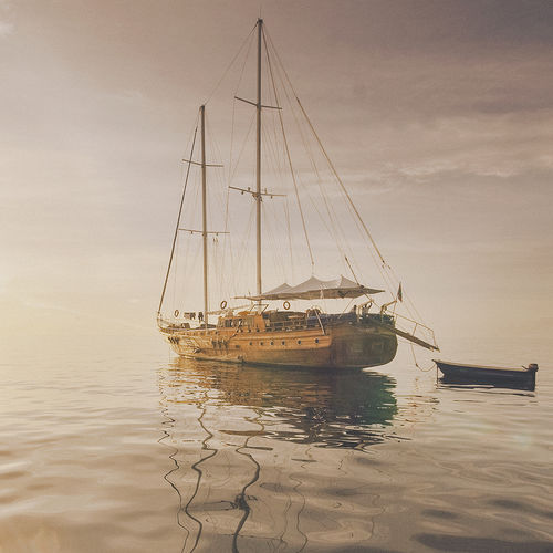 Fotografia de um barco com um aspecto retrô no mar. Há um pequeno barco a motor amarrado nele. O mar está calmo, mas há muita névoa.