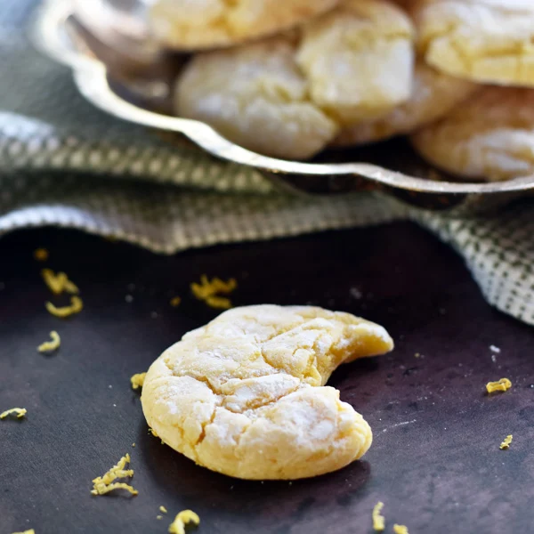 Bite shot of lemon cake mix cookie on sheet pan with lemon zest scattered around it