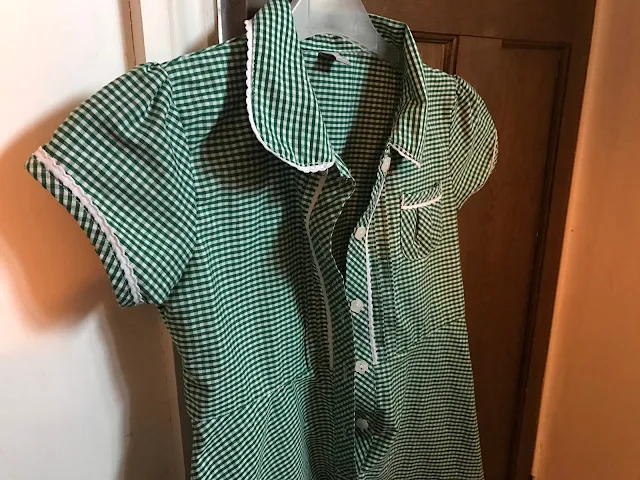 A green checked Sainsburys school summer dress with buttons hanging on a door handle