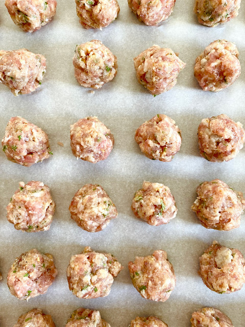 Uncooked meatballs lined up on parchment paper