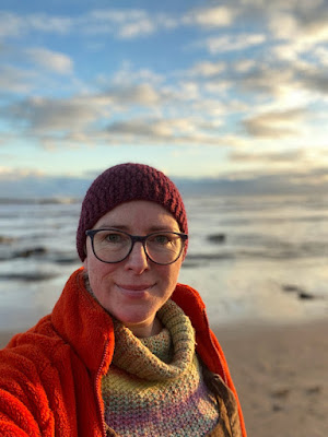 Selfie of a middle aged woman, on the beach, wearing a wooly hat, wooly jumper and fleecy coat