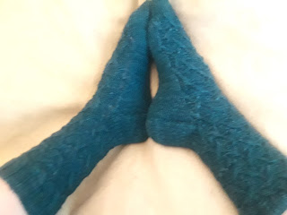 a pair of textured socks knit in a deep teal yarn.